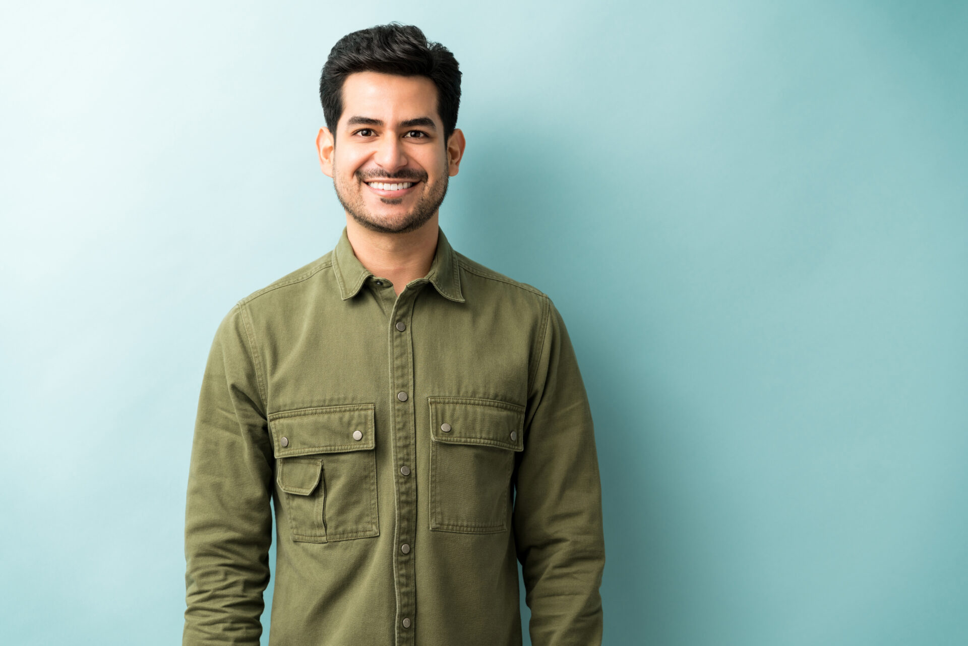 Handsome smiling man wearing green shirt standing against blue background